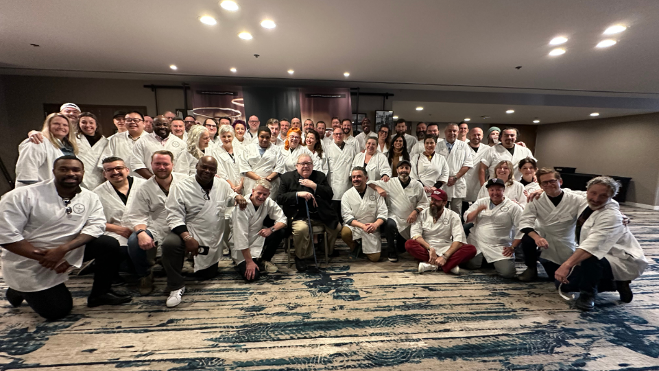 A man holding a glass of wine in a room filled with casks.